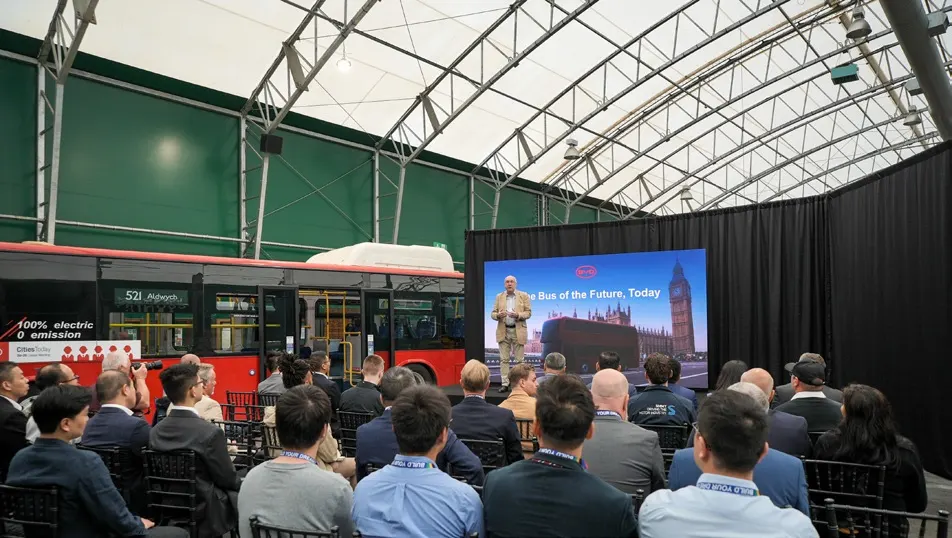 Audience seated beside a red double-decker bus during a presentation.
