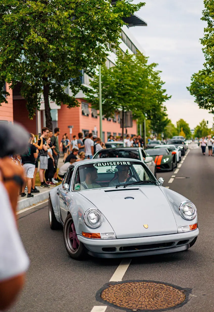 Sports car moving through a city street with spectators nearby.